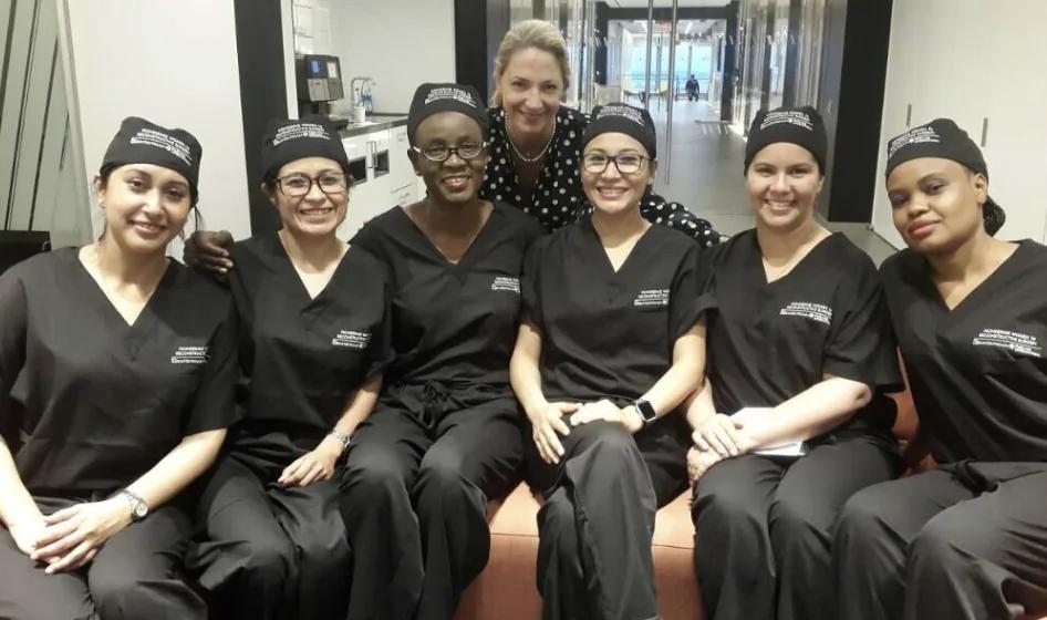 A cohort of the Pioneering Women in Reconstructive Surgery program, six surgeons in black scrubs and PWRS caps, seated together