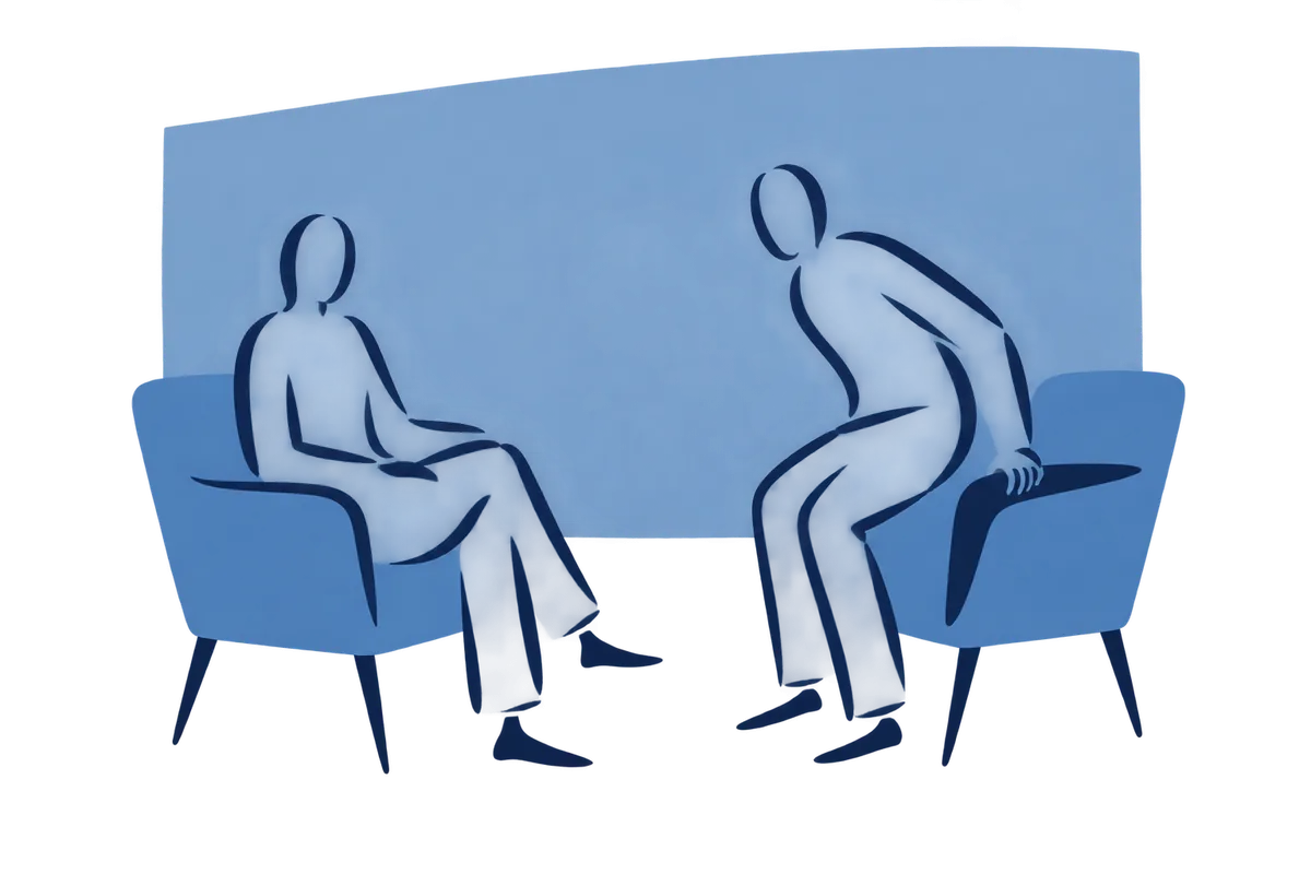 Two chairs turned towards each other, one person seated and one sitting down.